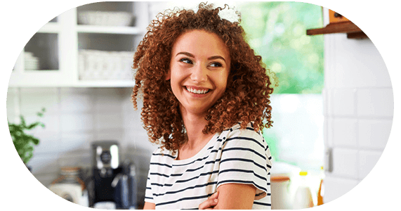 Mulher de cabelo cacheado, sorrindo e de braços cruzados.