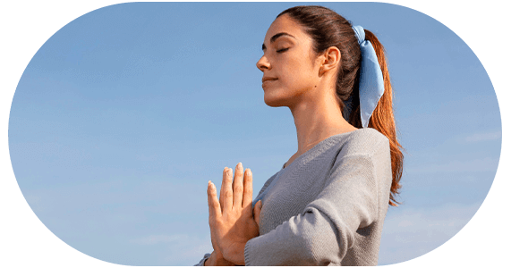 mulher praticando ioga ou meditação, suas mãos estão na frente do peito e seus olhos estão fechados.